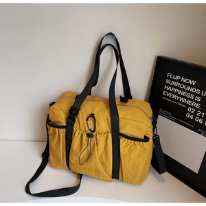 Detail of yellow nylon tote bag featuring functional drawstring pockets and a silver carabiner