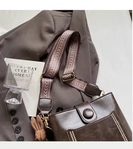 Detalle de bolso bucket marrón con correa ancha estampada y un colgante de conejo tejido