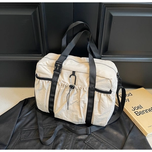 Close-up of cream nylon tote bag with drawstring side pocket and durable black straps