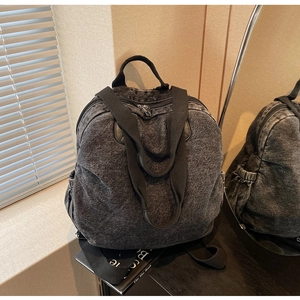 Detail of grey washed denim backpack with adjustable straps and side pockets on a desk