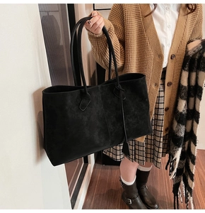 Close-up of a black matte tote bag featuring long leather handles and a minimalist charm