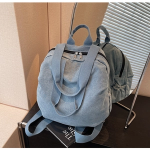 Close-up of light blue denim backpack with silver dual zippers and fabric texture details
