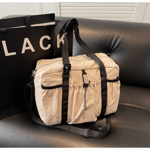 Close-up of a large beige nylon tote bag on a black leather sofa with a metal carabiner detail