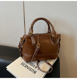 Detail of a brown Boston bag with white contrast stitching and gold-tone hardware