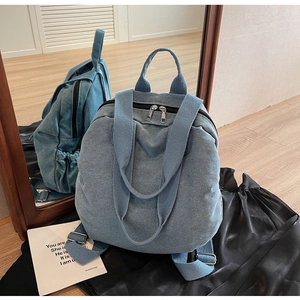 Rear view of denim canvas backpack showing adjustable straps and silver zippers in mirror reflection