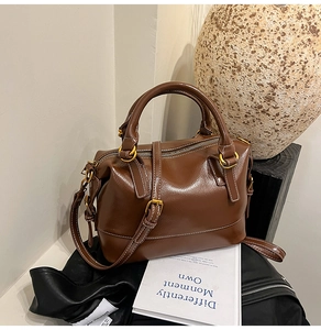 Close-up of brown glossy Boston bag with white stitching and golden metal hardware