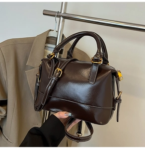 Detail of dark brown leather Boston bag with white contrast stitching and gold hardware