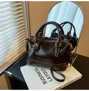 Detailed view of coffee brown faux leather handbag with white contrast stitching and gold hardware
