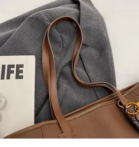 Close-up of brown litchi grain PU leather bag showing long shoulder straps and gold ring detail