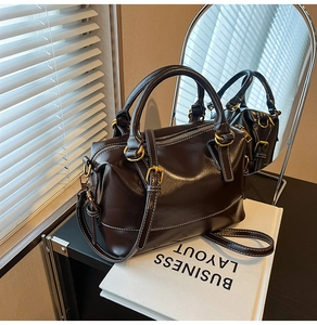 Detail of dark brown leather Boston bag with white stitching and gold hardware accents