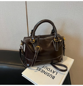 Detailed view of deep brown glossy Boston bag featuring contrast white stitching and gold hardware