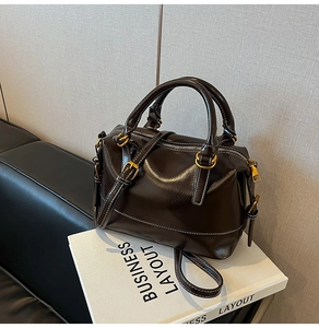 Detailed macro of dark brown leather Boston bag with contrast white stitching and gold hardware