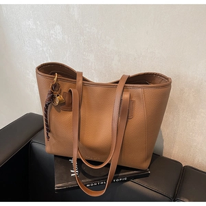 Close-up of caramel brown pebble leather tote bag with gold logo and decorative keychain