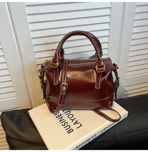 Detail of burgundy Boston bag showing white contrast stitching and gold metal zippers