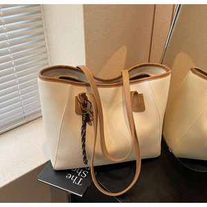 Detail of a large cream leather tote bag with brown contrast handles and litchi texture