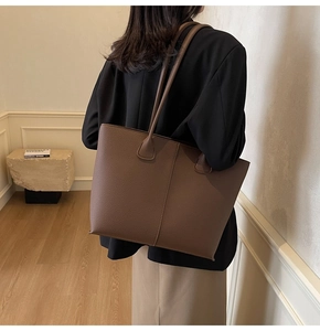 Detail of dark brown lychee leather texture and vertical stitching on tote bag