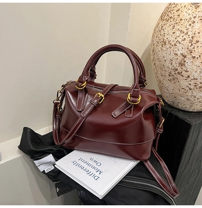 Detail of burgundy leather Boston bag with gold buckles and detachable shoulder strap