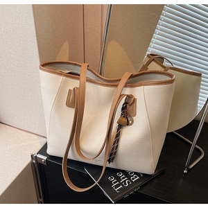 Detail of cream lychee leather tote bag with brown straps and side metal charm