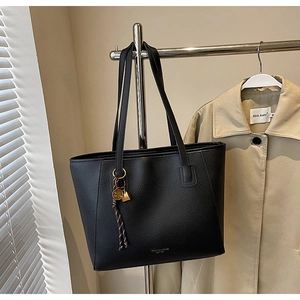 Detail of black pebbled leather tote bag with gold disk tassel charm and thin straps