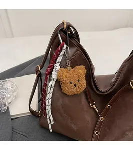 Detail of a brown plush bear keychain with a metal clasp on a vintage faux leather tote