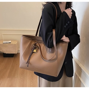 Detailed view of brown lychee leather tote bag with gold logo and woven pendant