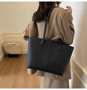 Close-up of black pebble leather tote bag with vertical stitching detail and long handles
