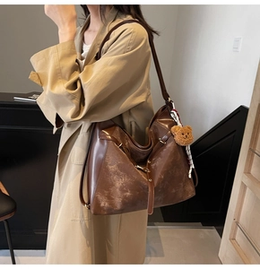 Detail of vintage dark brown tote bag with decorative side buckles and plush bear charm