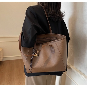 Detailed side view of a large brown leather tote bag with braided charm on a model