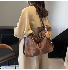 Detail of a brown hobo shoulder bag with a plush bear charm on a model in a trench coat
