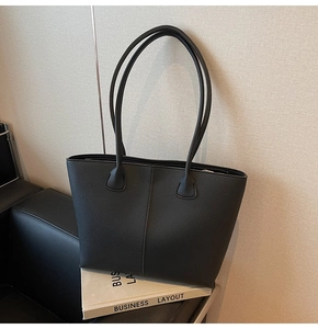 Detail of black pebbled leather tote bag with vertical stitching on a sofa