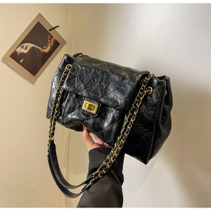 Close-up of black quilted leather shoulder bag with gold chain and metal clasp detail