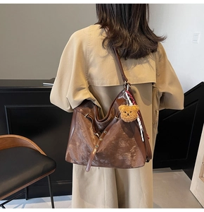 Detail of large brown crossbody bag with retro texture and a cute bear charm pendant