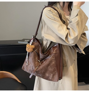Detail of vintage dark brown crossbody bag with plush bear charm and ribbon accent