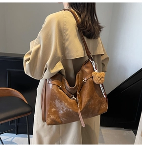 Detail of cognac leather tote bag with plush bear charm and striped scarf on shoulder strap