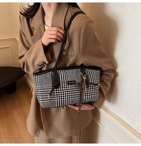 Nahaufnahme der Hahnentritt-Tasche mit Metalllogo und Quastenanhänger auf braunem Blazer