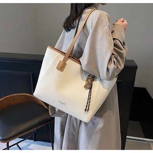 Detail of a cream faux leather tote bag with brown handles and elegant brand text