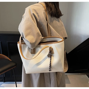 Detail of cream lychee leather tote bag with brown straps worn by a model in lifestyle setting