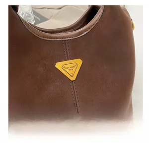 Gros plan d'un sac en cuir mat marron avec logo triangulaire doré et détails de double couture