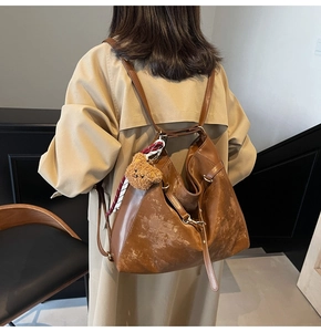 Detail of large brown tote bag with plush bear charm and plaid scarf accent