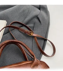 Detail of retro brown handbag featuring adjustable strap and gold metal hardware buckles