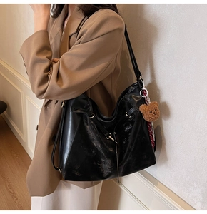 Detail of black leather tote bag with golden hardware, teddy charm, and silk scarf