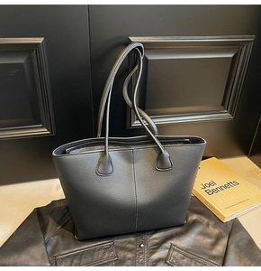 Close-up of black textured leather tote bag with vertical stitching and strap detail