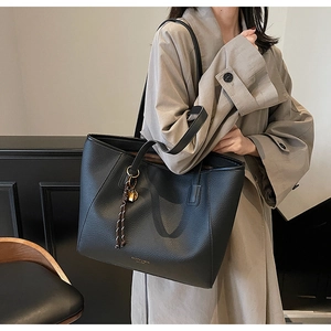 Detail of black pebbled leather tote bag with elegant golden padlock and woven strap charm