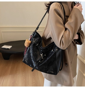 Close-up of black leather tote bag with a brown plush bear charm and ribbon detail