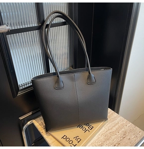 Close-up of black pebbled leather tote bag with vertical stitching on marble surface