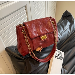 Detail of burgundy quilted leather handbag with gold metal clasp and chain strap