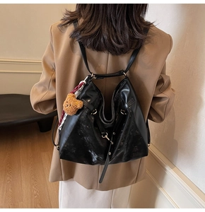 Detail of black faux leather tote with brown plush bear charm and checkered ribbon strap