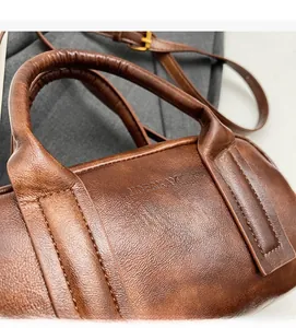 Close-up of brown leather cylinder handbag showing fine texture and embossed brand logo