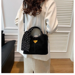 Détail d'un sac à main noir mat avec logo triangle doré et poignée en foulard à pois