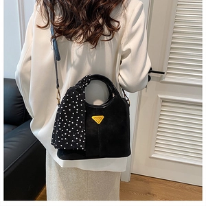 Détail d'un sac seau noir mat avec logo triangle doré et foulard en soie à pois élégant